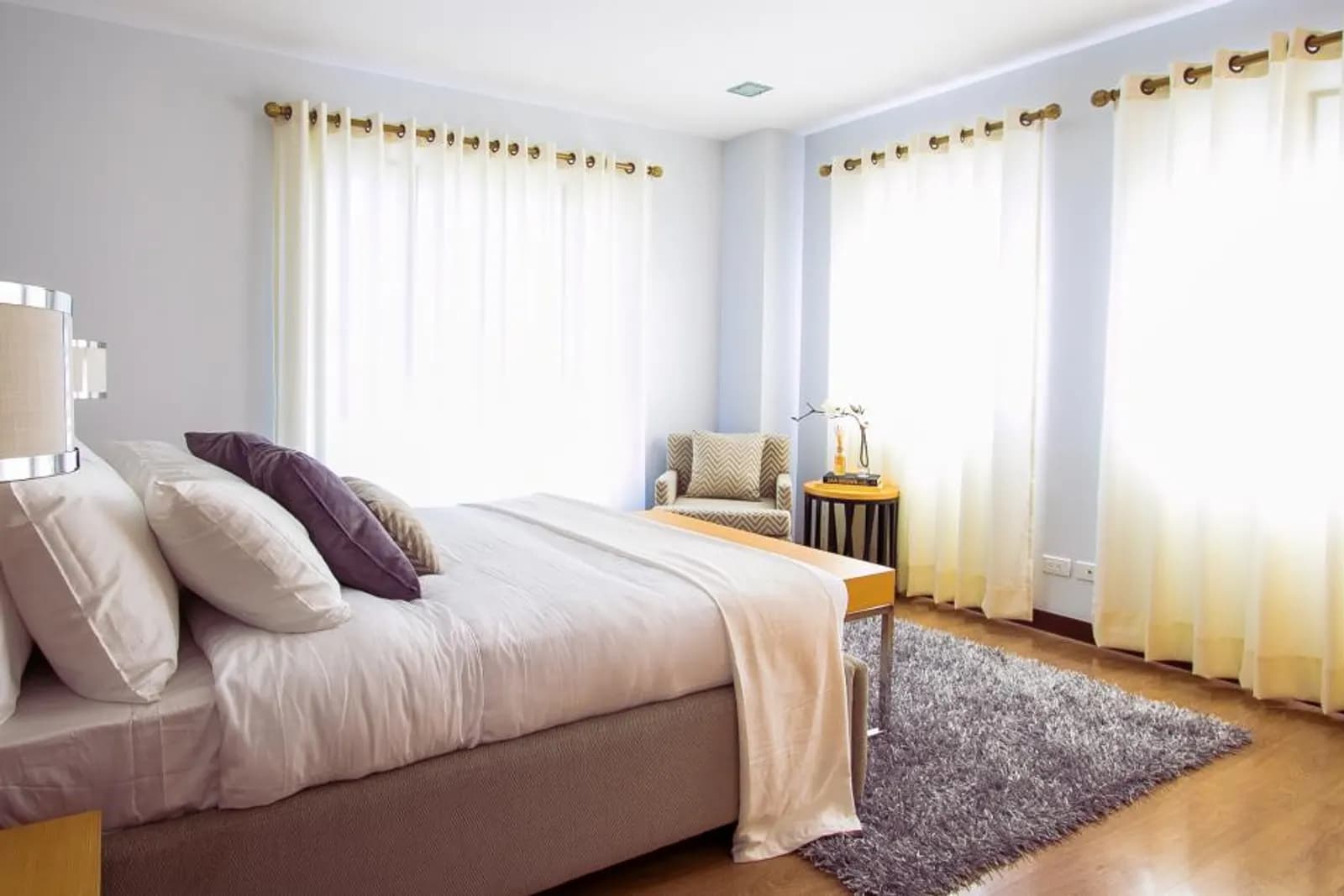 Bedroom with floor-length eyelet curtains hung on rods above two windows
